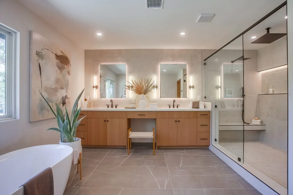 Completed primary bathroom with lit vanity mirrors, recessed ceiling lighting, and glass shower
